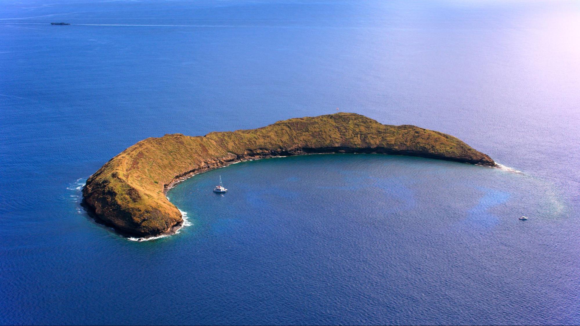 Aerial view of crescent-shaped Molokini Crater volcanic islet surrounded by deep blue Pacific Ocean waters near Maui