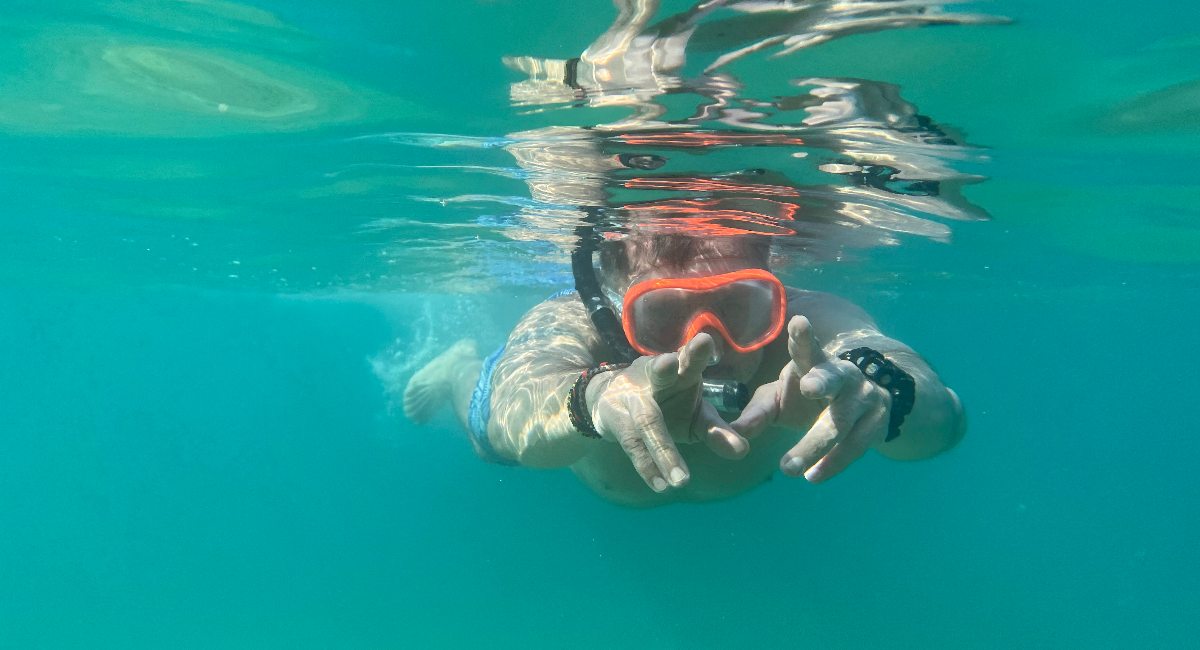 An adult man is seen swimming in clear turquoise water, wearing a snorkel mask and breathing tube.