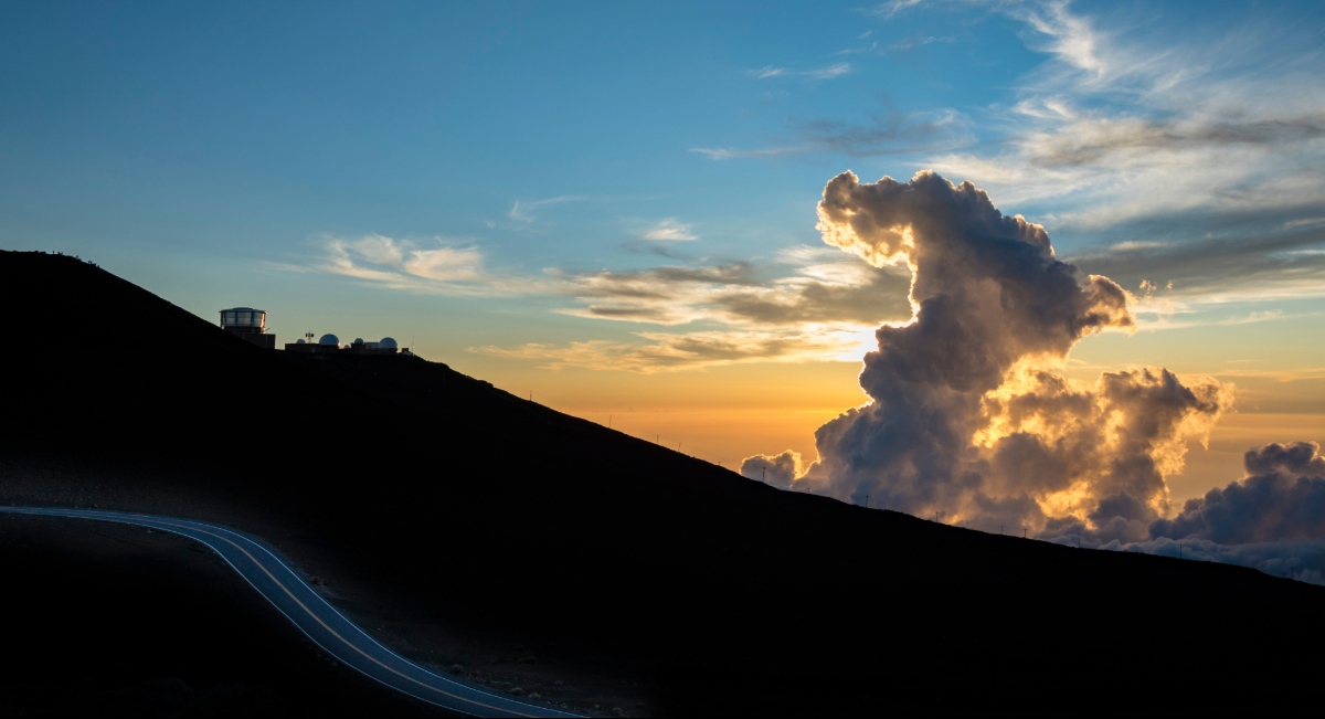 Pre-dawn sky above the Haleakala summit with golden clouds and a winding road on the mountain slope — Haleakala National Park, Maui